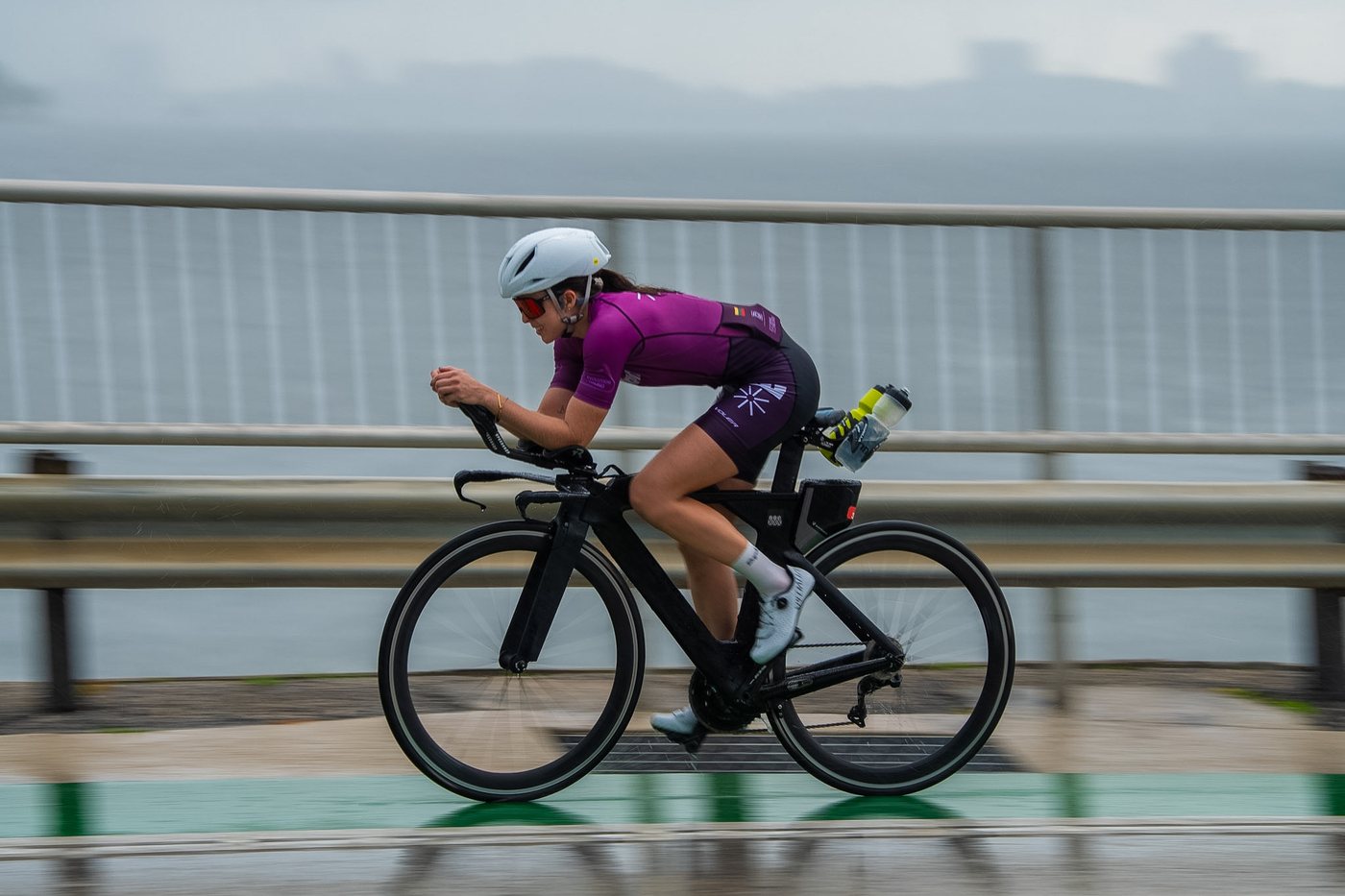 A cyclist riding fast in side profile along a coastal road.